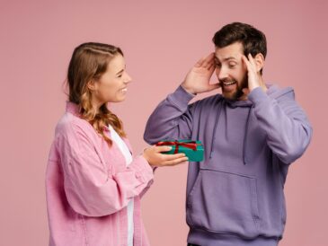 Smiling woman holding gift box for her lovely boyfriend at punk background